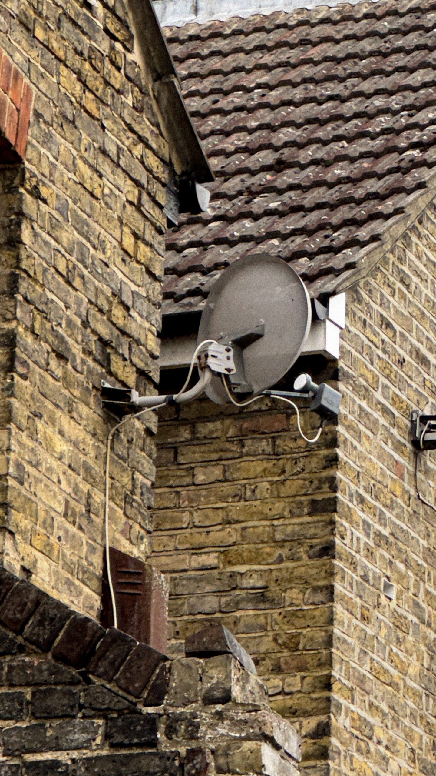 Close-up of a satellite dish and security light mounted on the yellow brick corner of 334 High Street in Chatham, Kent
