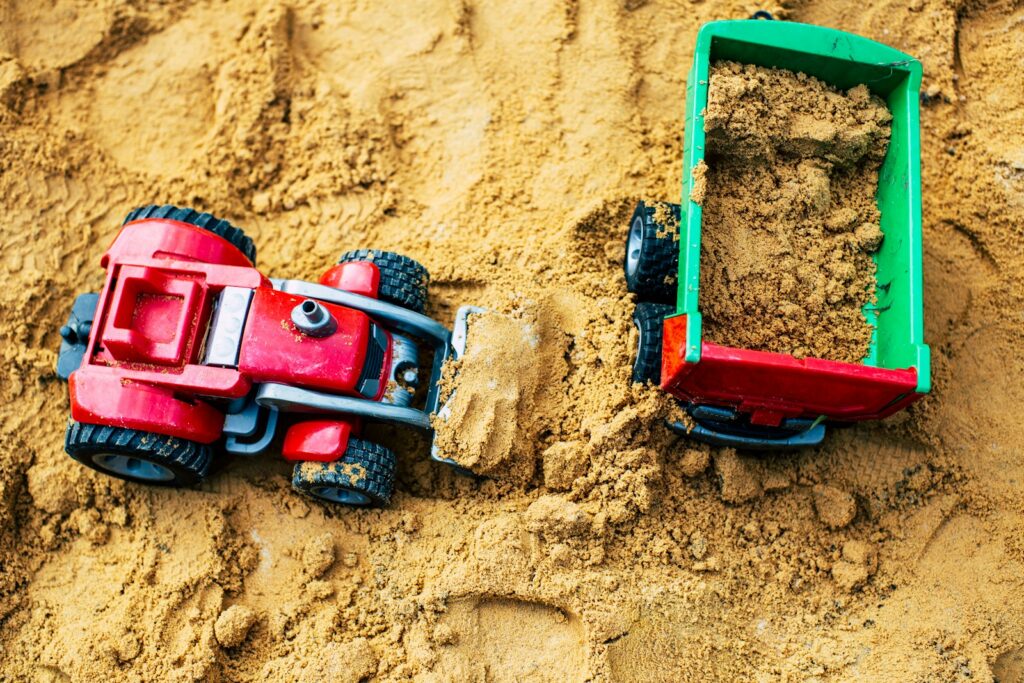a red toy truck and a green toy car are in the sand