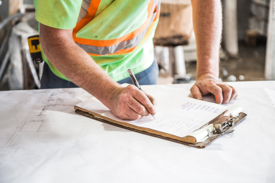 Warehouse worker writing notes on a clipboard over printed plans